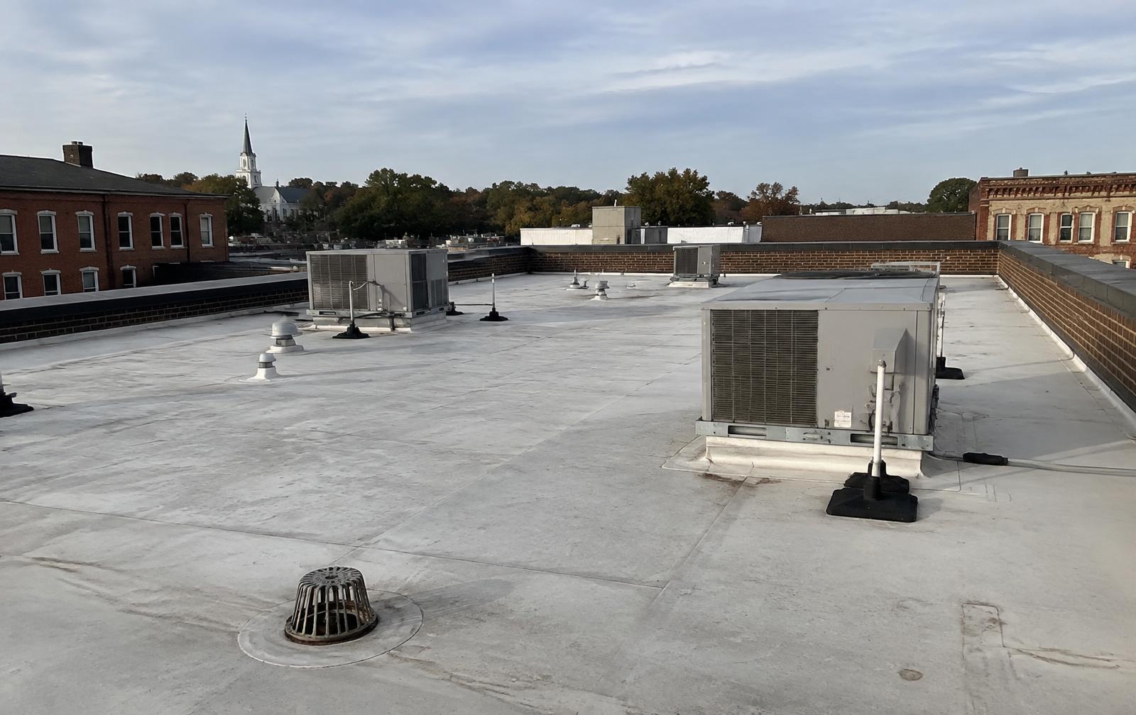 Low slope commercial membrane roof with rooftop mechanical units, vent stacks and a roof drain, surrounded by a brick parapet wall