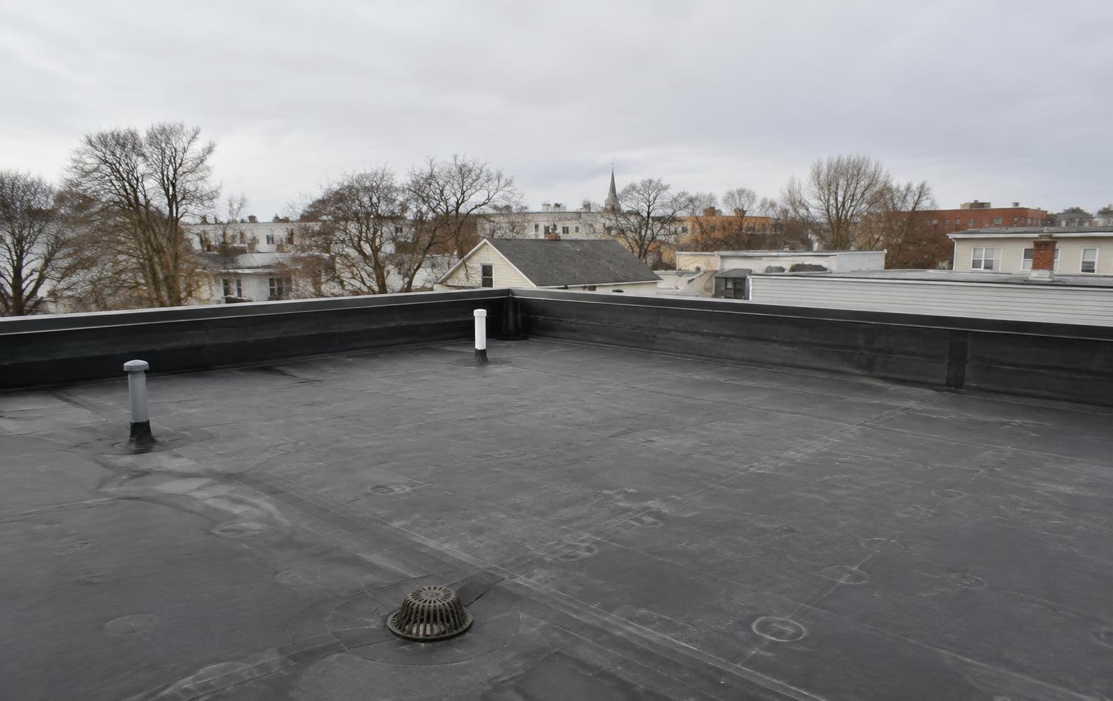 Flat black rubber membrane roof on a multi family building, with a centre roof drain, vent pipes and a wrapped parapet edge